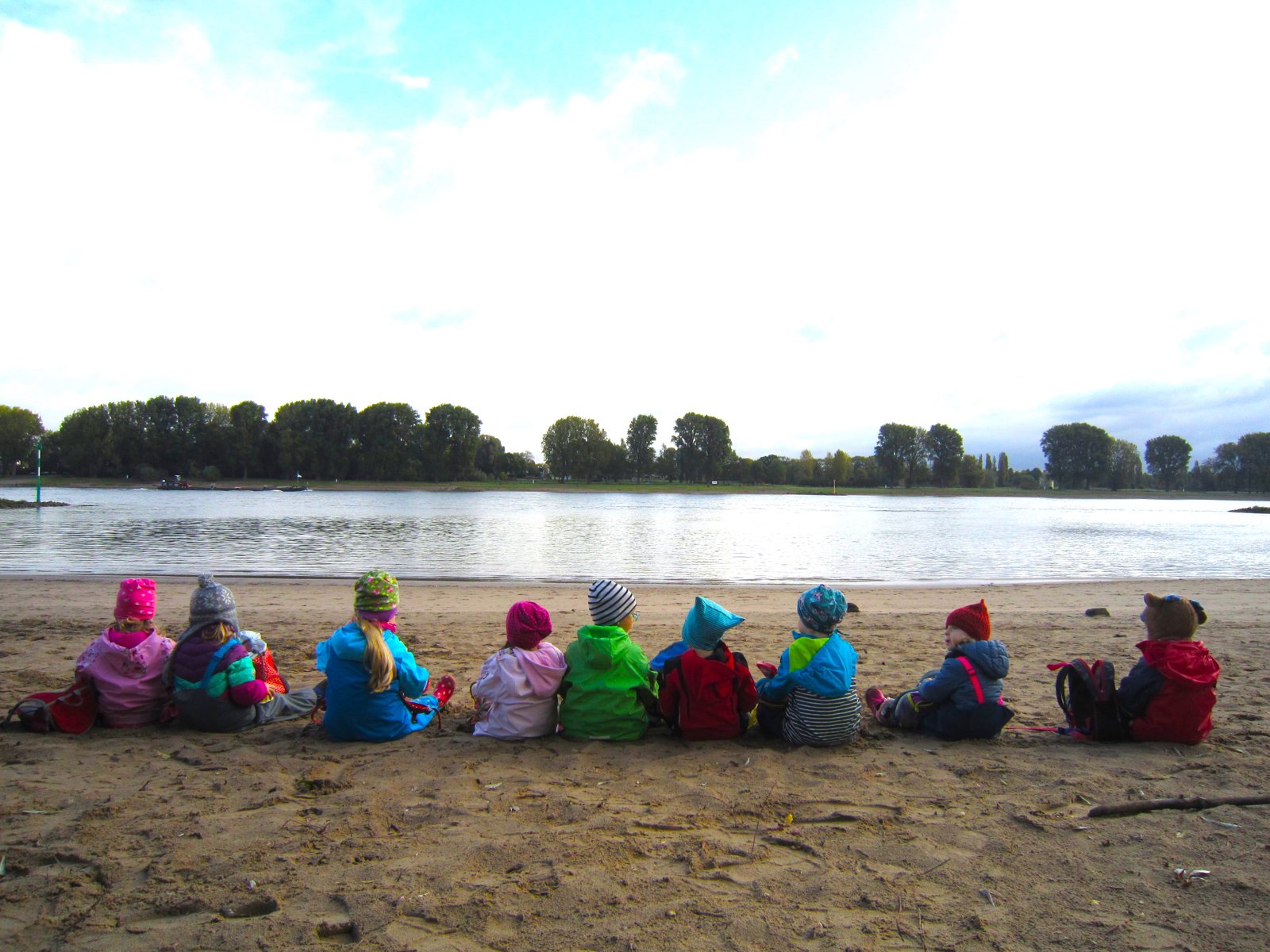 Children sitting in a row on the bank of the Rhine looking at the water