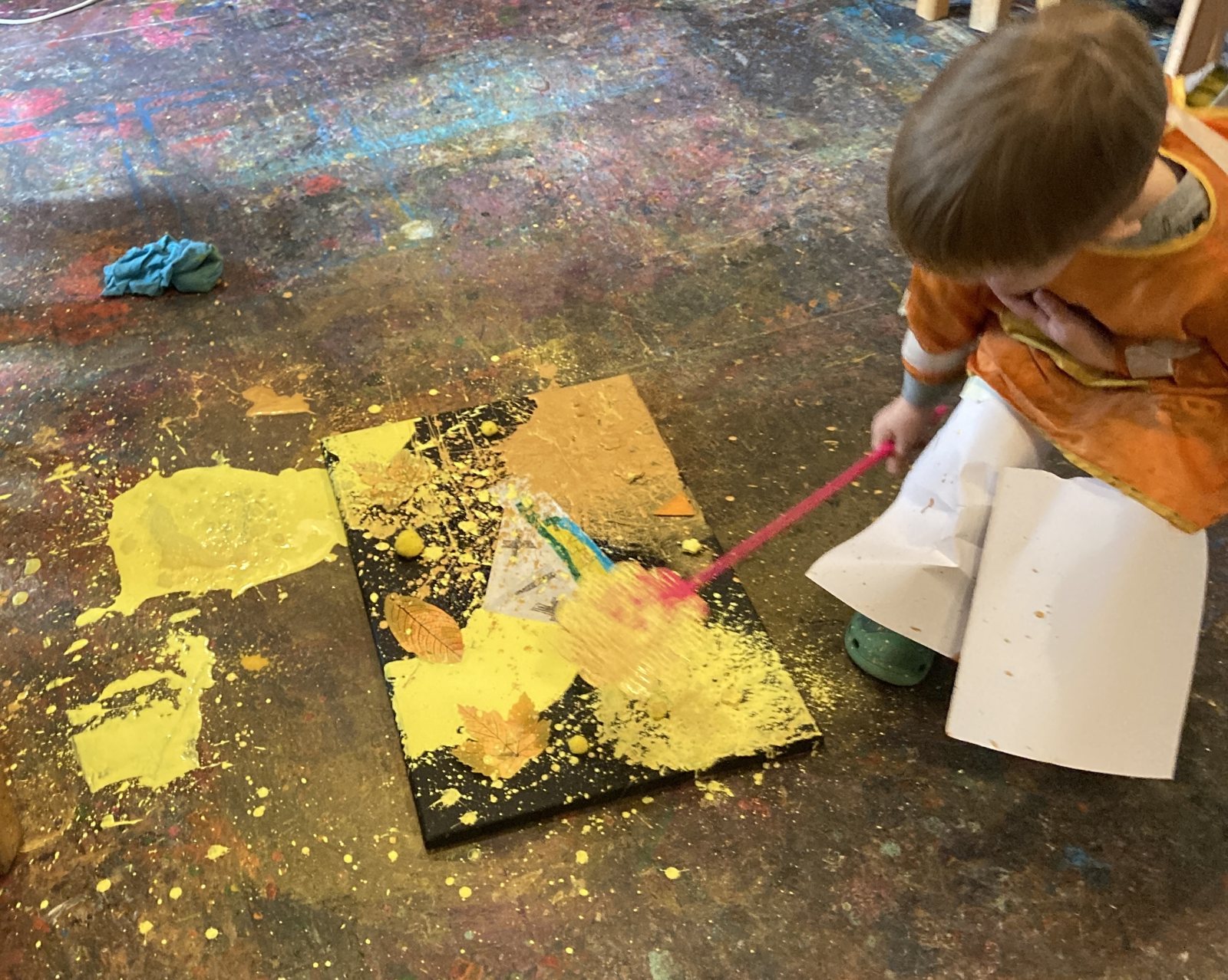 A child creating a picture with yellow paint and autumn leaves