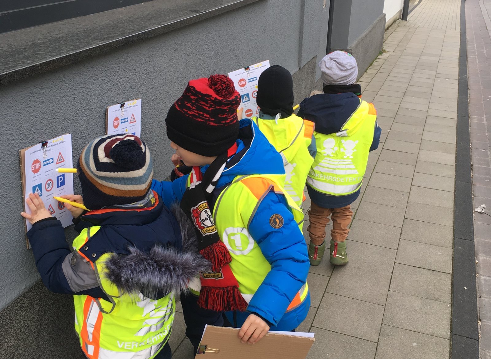 Children in high-visibility vests looking for traffic signs